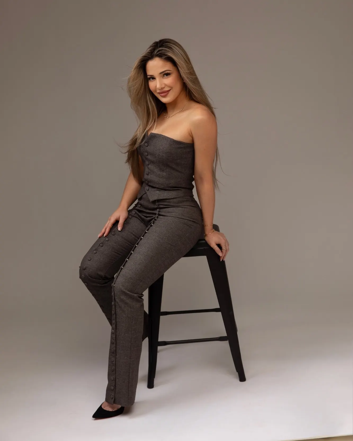 Katherine Oganesyan, RN, seated on a stool in a tailored grey set, photographed against a plain backdrop